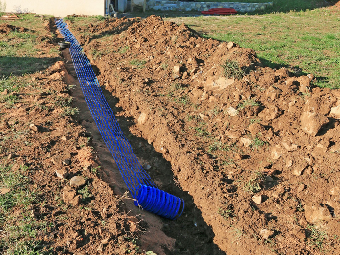 Tuyau de drainage bleu posé dans une tranchée de terre, dans un jardin.