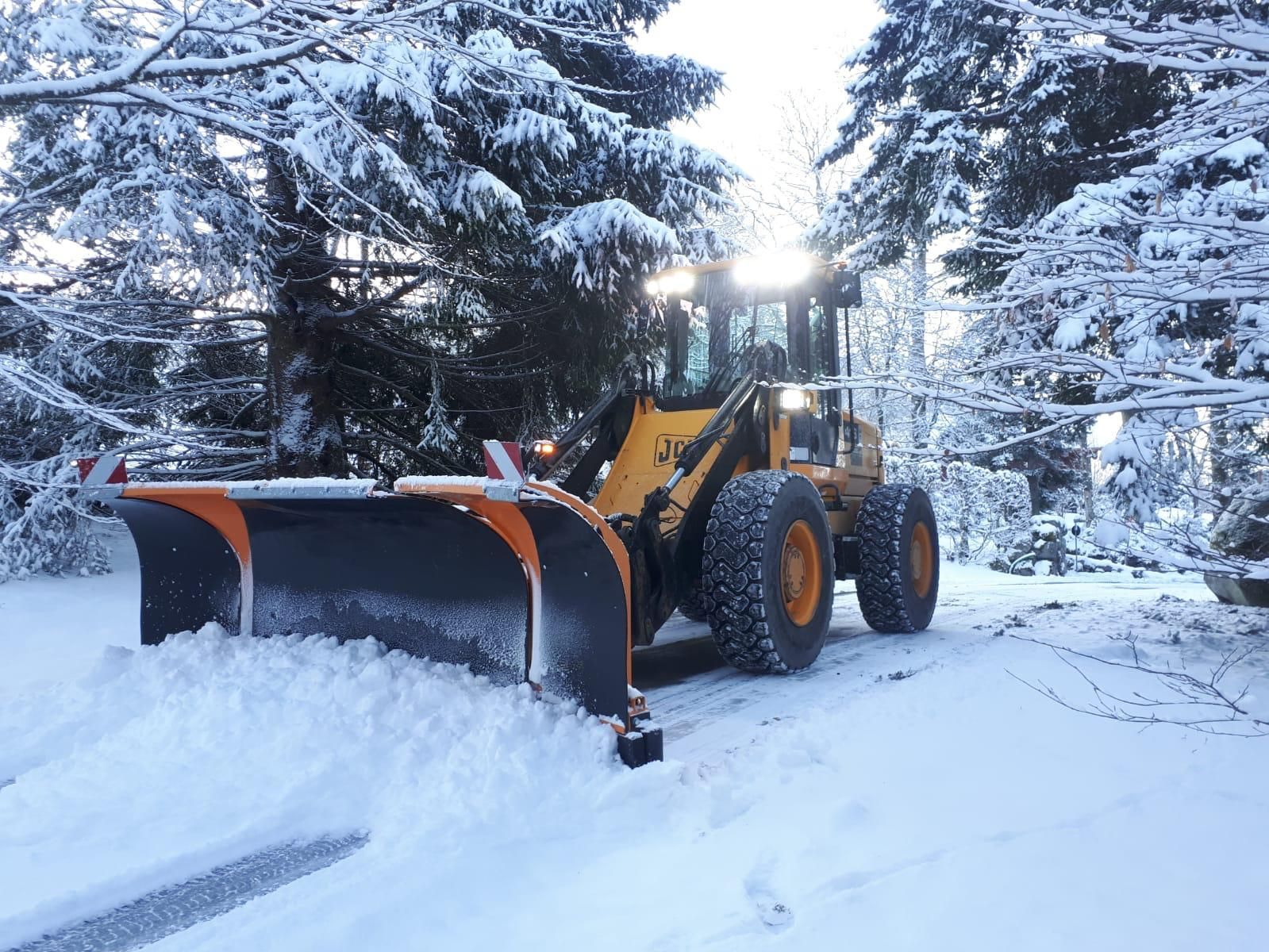 Un chasse-neige jaune dégageant une route enneigée dans une forêt au crépuscule.