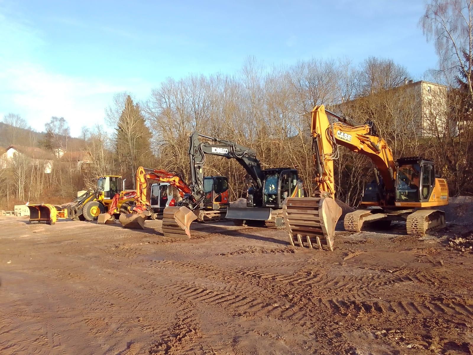 Chantier de construction avec des excavatrices sur un terrain en terre, sous un ciel bleu dégagé.