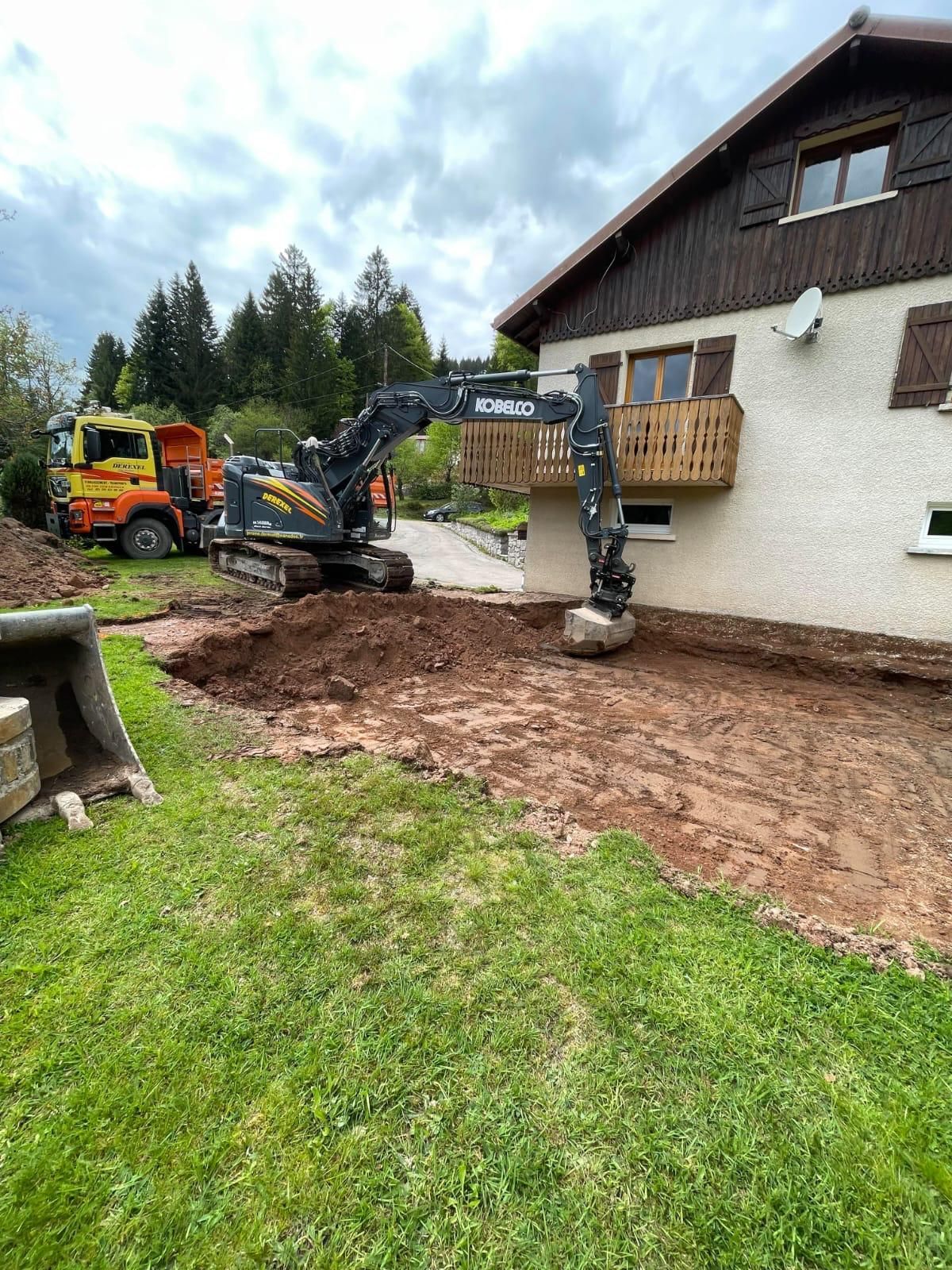 Une excavatrice creuse le sol à côté d’une maison.