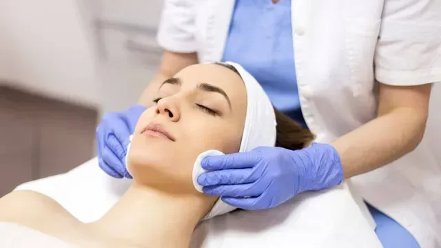 Mulher recebendo tratamento facial em uma clínica. A esteticista usa discos de algodão em seu rosto.