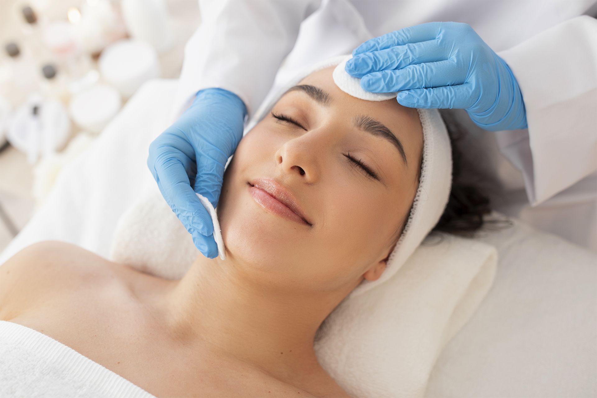Mulher recebendo tratamento facial em uma clínica. A esteticista usa discos de algodão em seu rosto.