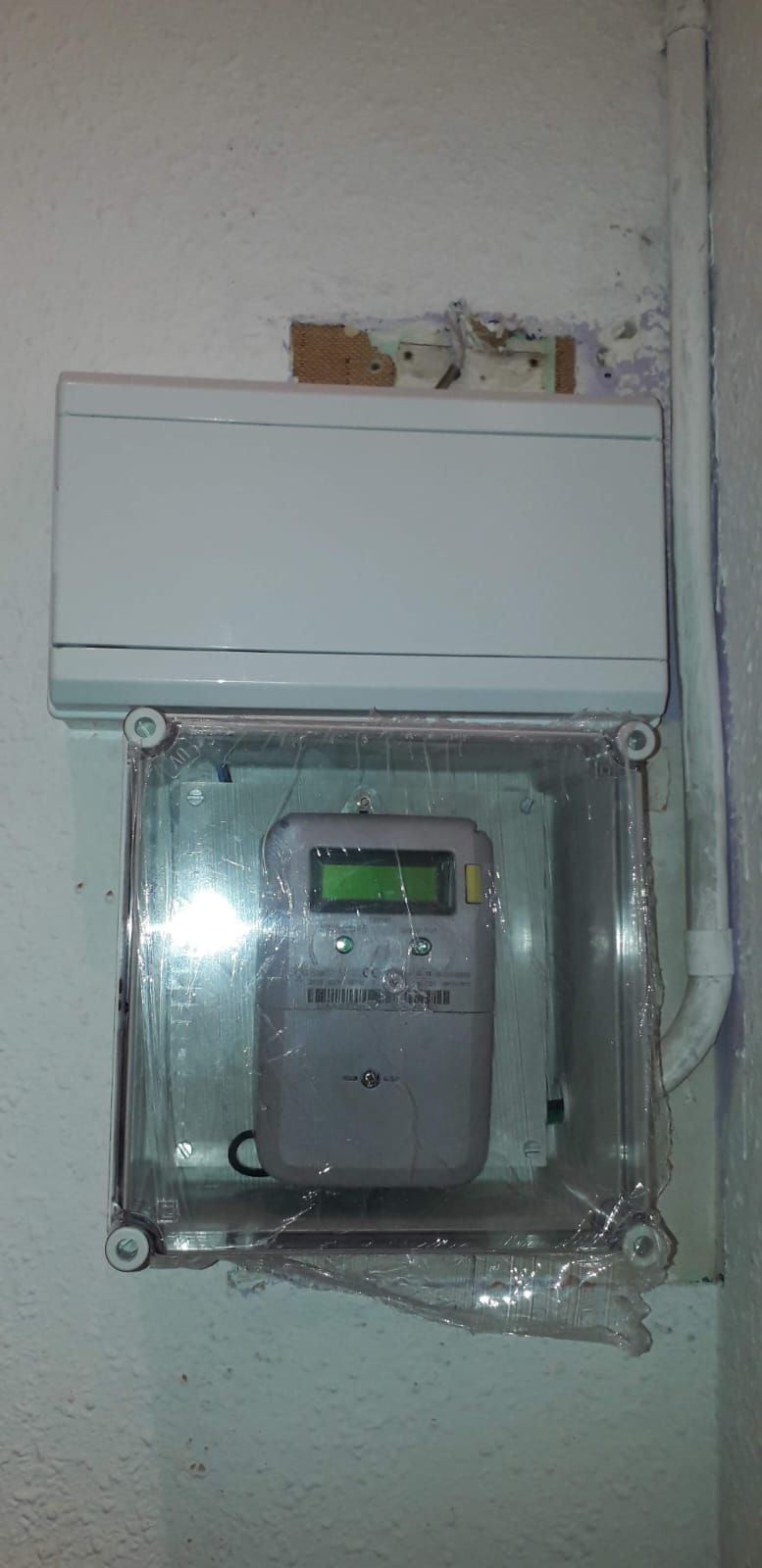 Un reloj digital está dentro de una caja de plástico transparente en una pared.