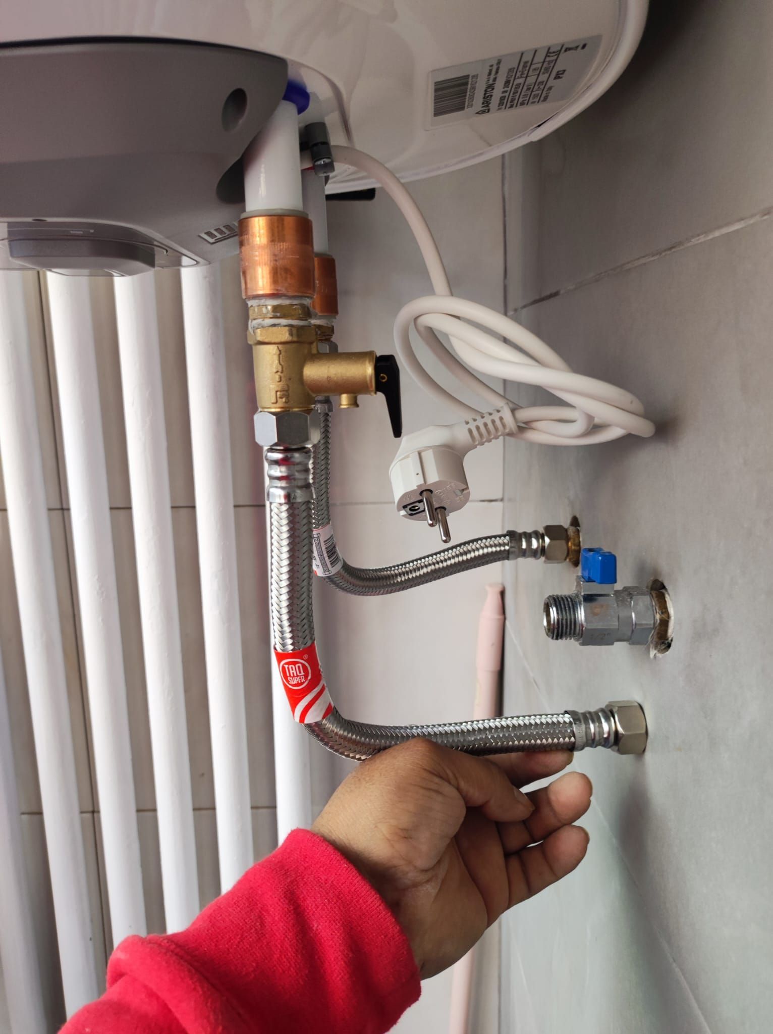 Una persona está arreglando un calentador de agua con una manguera conectada a él.