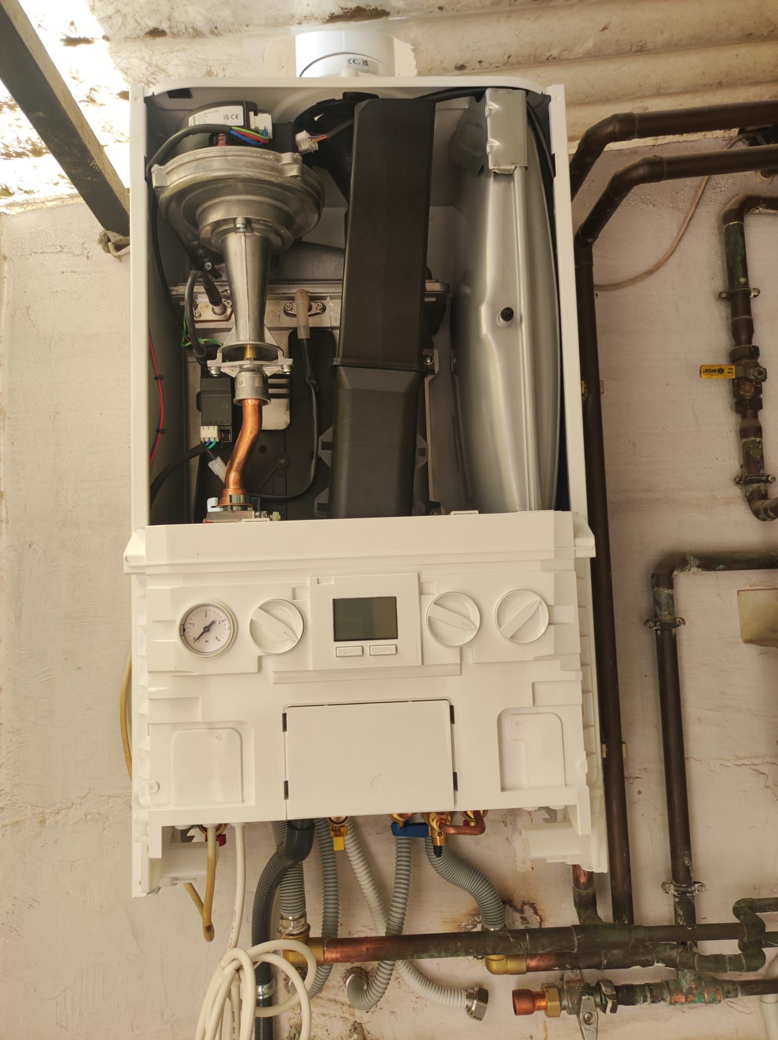 Una caldera blanca está colocada en una pared al lado de unas tuberías.