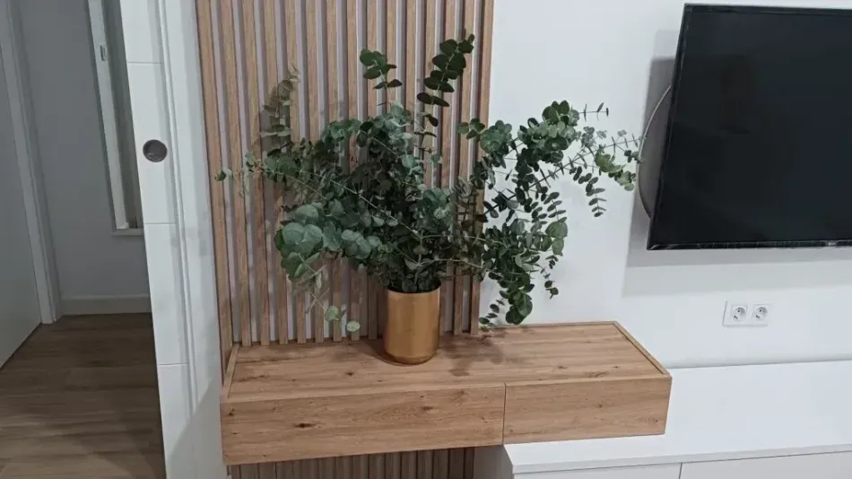 Estantería de madera con una planta frondosa en maceta junto a un televisor montado en la pared en una habitación moderna.
