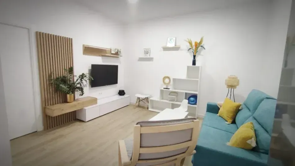 Sala de estar moderna con sofá color turquesa, televisor, estantes blancos y muebles de madera clara.