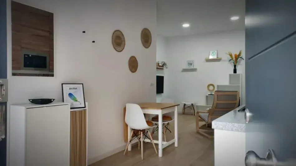 Espacio habitable moderno y minimalista con paredes blancas, muebles de madera y un pequeño comedor cerca de la cocina.