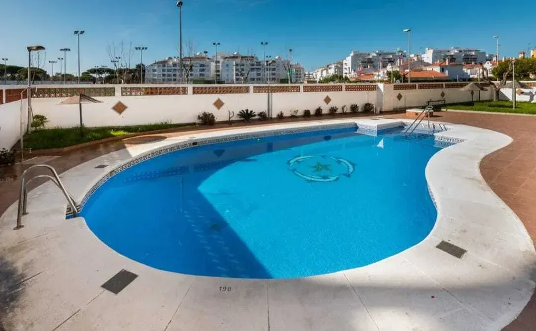 Piscina exterior con agua azul y terraza blanca en un complejo residencial.