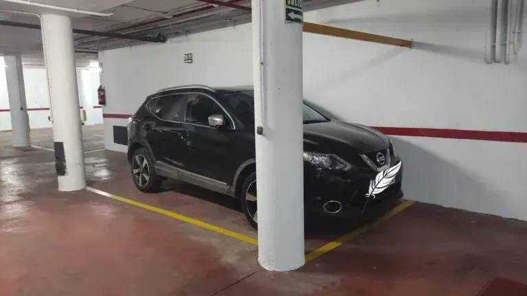 Un SUV negro estacionado en un garaje subterráneo entre pilares blancos y líneas amarillas de aparcamiento.