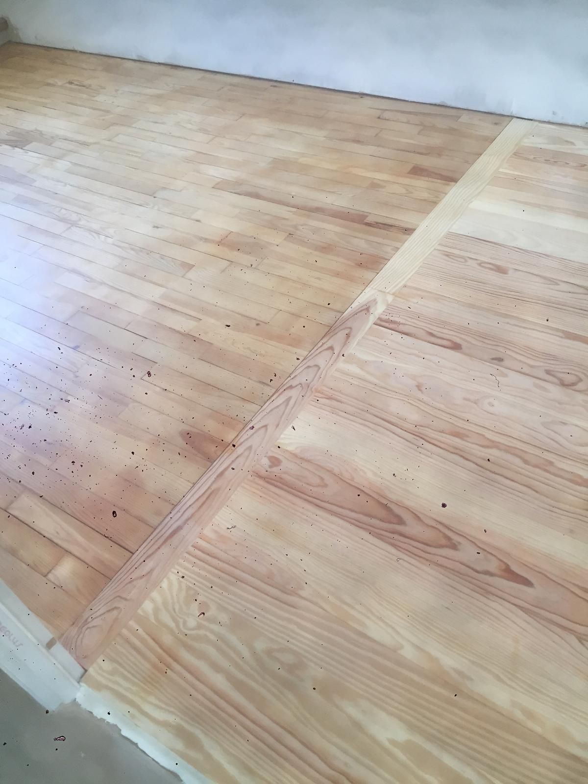 Plancher en bois dans une pièce, avec une ligne diagonale séparant les parties poncées et non poncées.