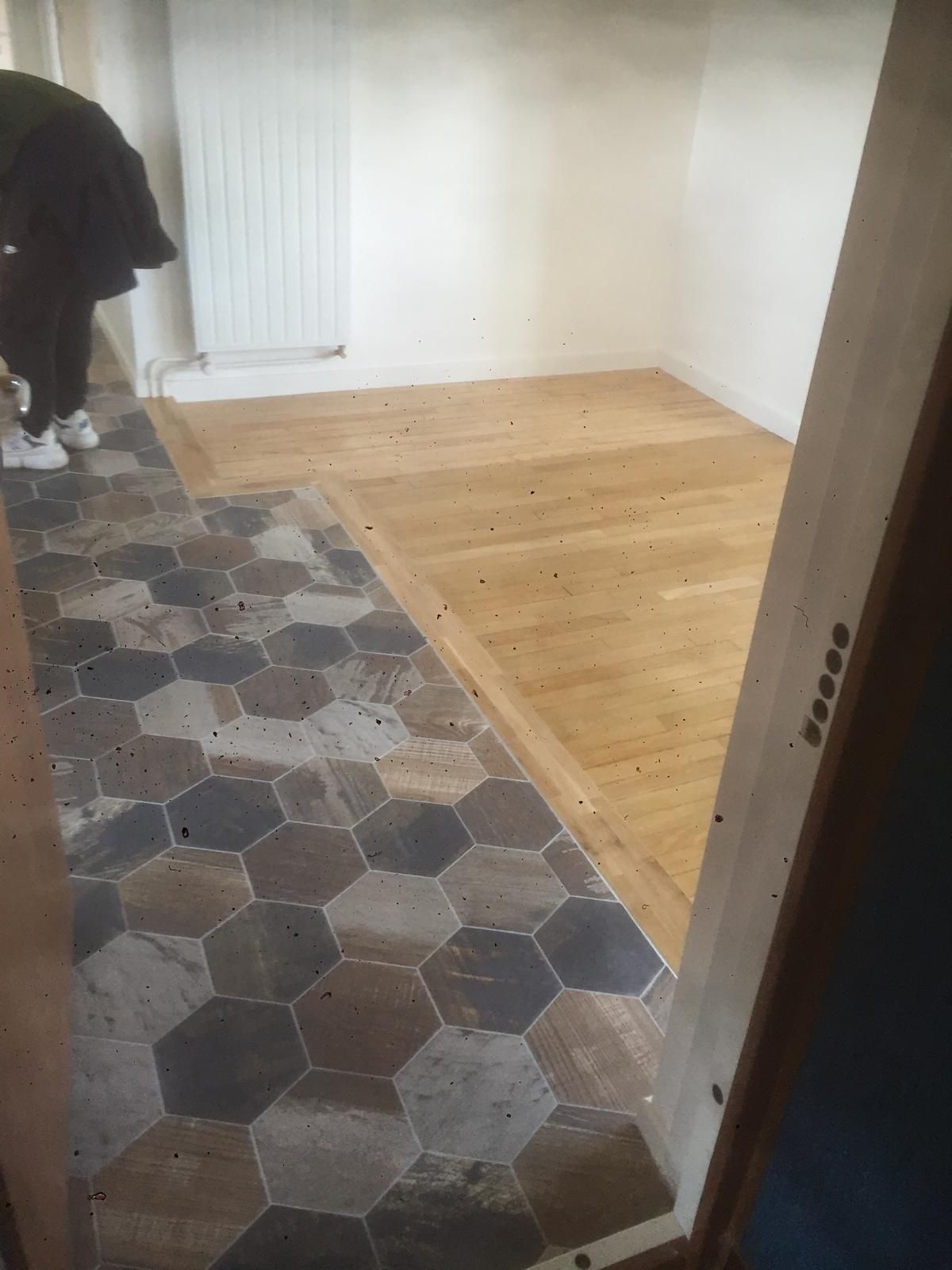 Une personne se tient près d'une porte. Un côté du bâtiment est carrelé de carreaux hexagonaux, l'autre côté est recouvert d'un parquet.