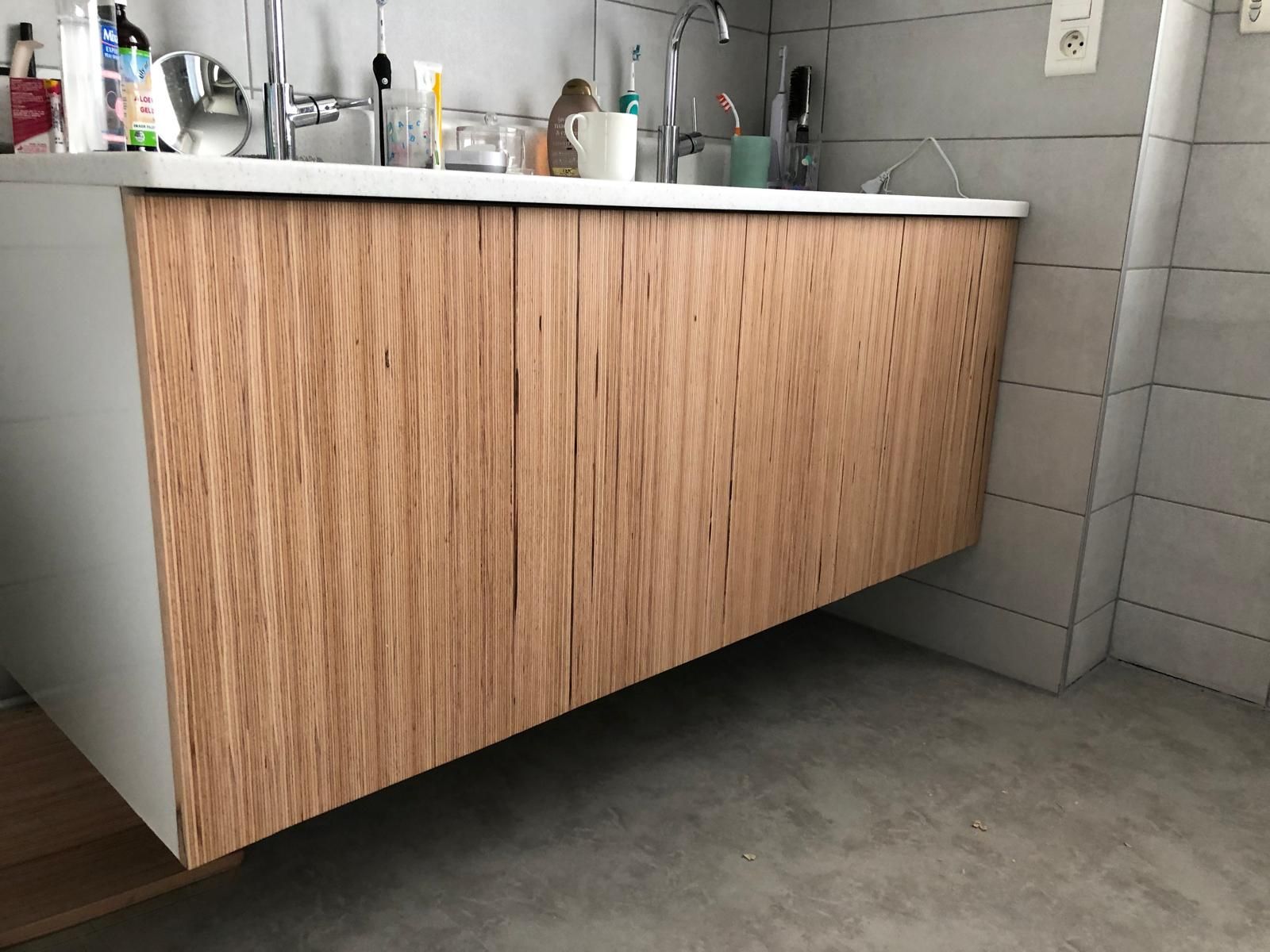 Meuble-lavabo suspendu en bois avec comptoiret divers articles de toilette.