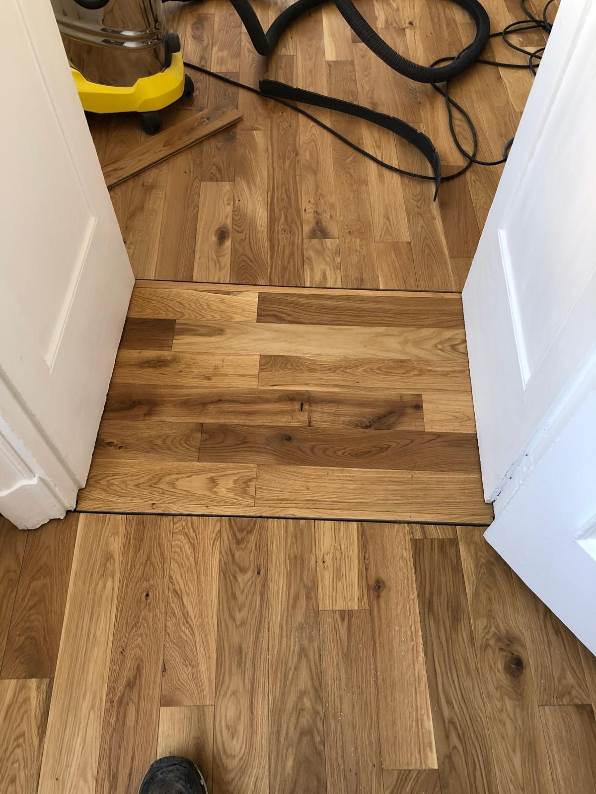 Parquet entre deux portes, séparées par un espace au centre. Un aspirateur est visible en arrière-plan.