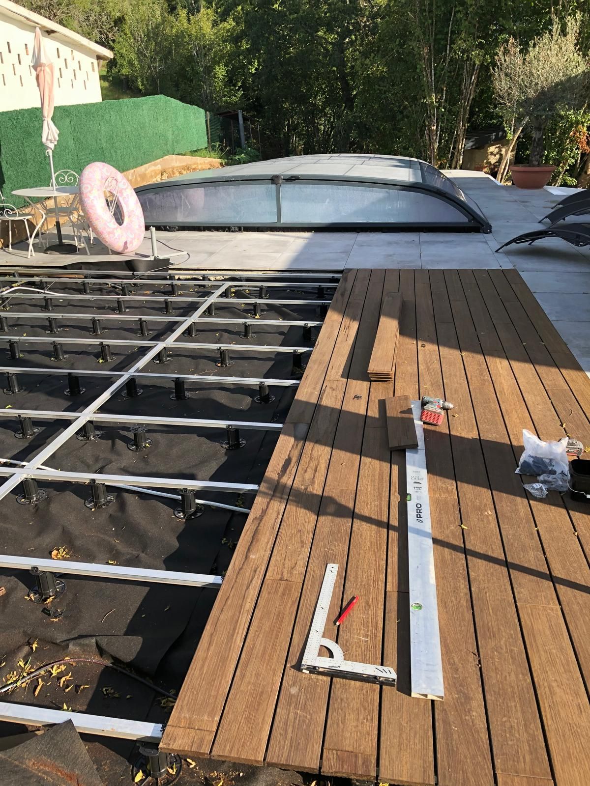 Construction de la terrasse : Planches de bois posées sur une structure métallique, près d'un abri de piscine et d'un patio.