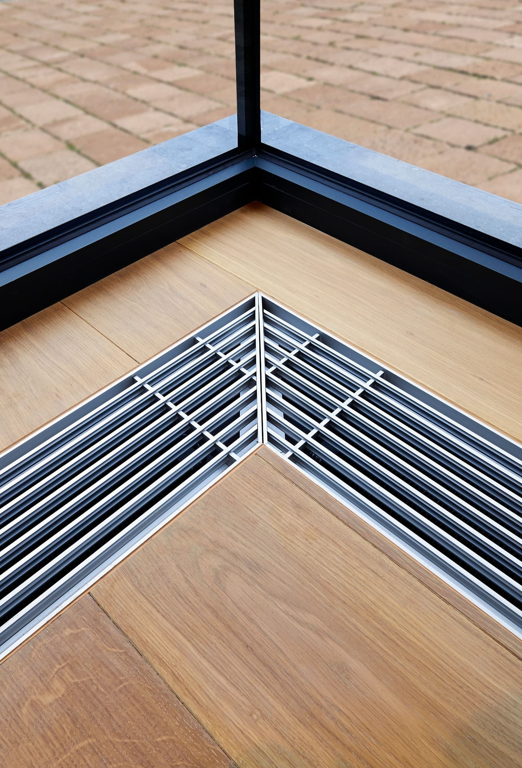 Un primer plano de una rejilla de metal sobre un piso de madera al lado de una ventana.