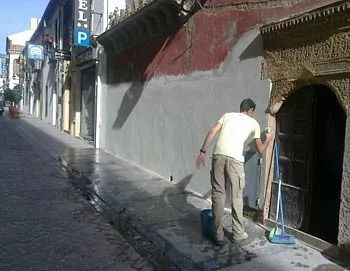 Un hombre está limpiando la acera frente a un edificio con la letra p.