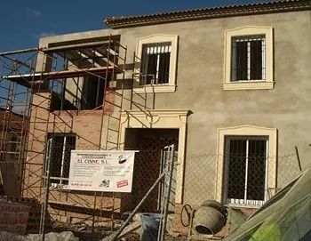 Se está construyendo una casa con andamios alrededor y un cartel al costado.