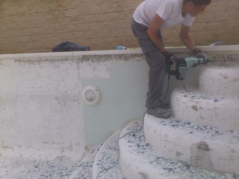 Un hombre está trabajando en una piscina con un taladro.