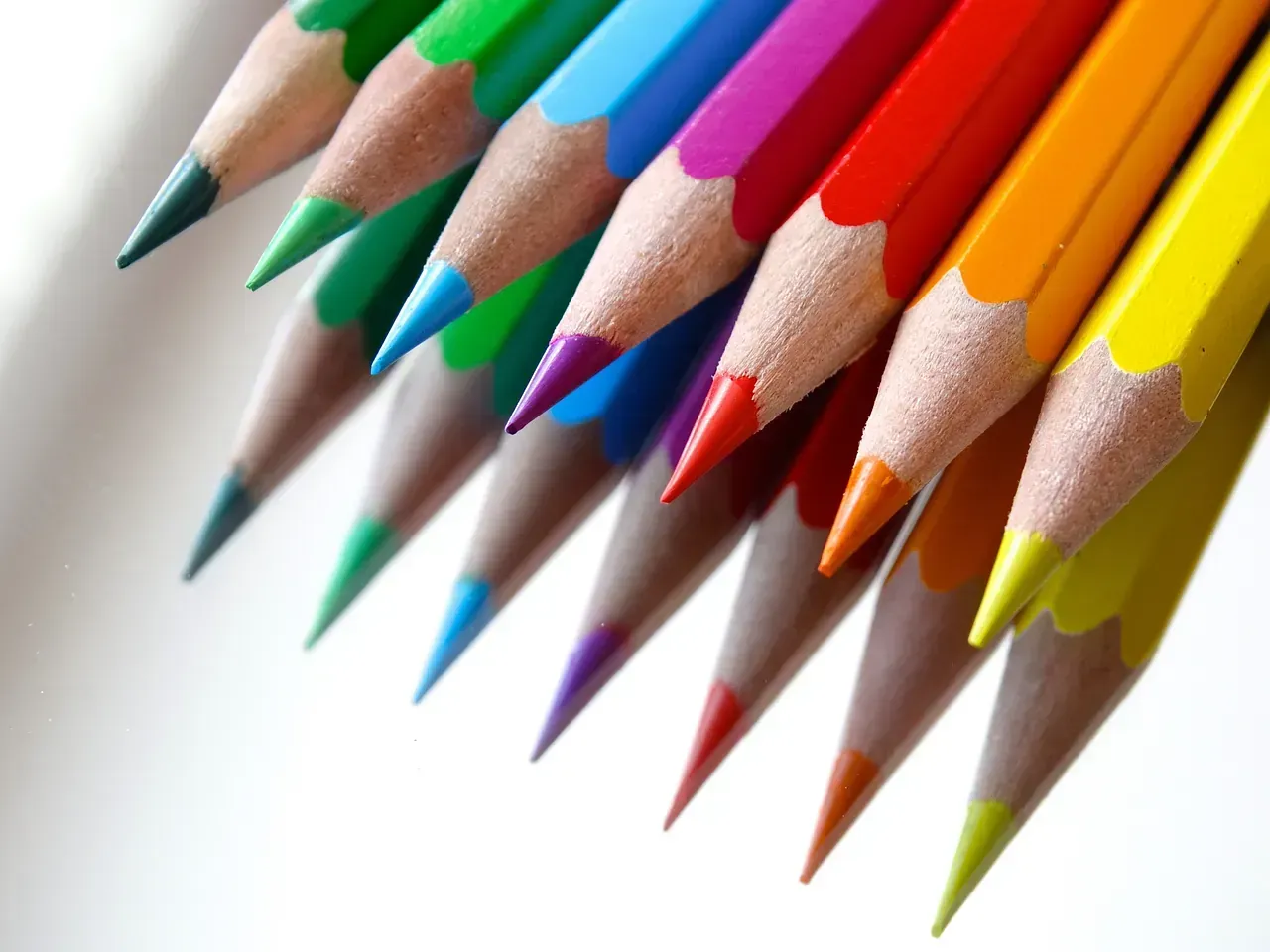 Primer plano de lápices de colores afilados dispuestos en una línea diagonal, con puntas que muestran un arco iris de colores.