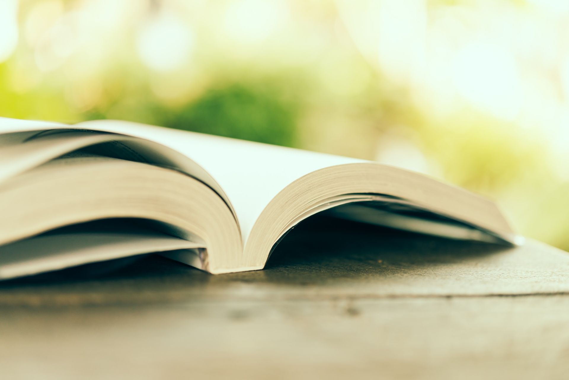 Libro abierto con páginas desplegadas sobre una superficie de madera, fondo verde borroso.