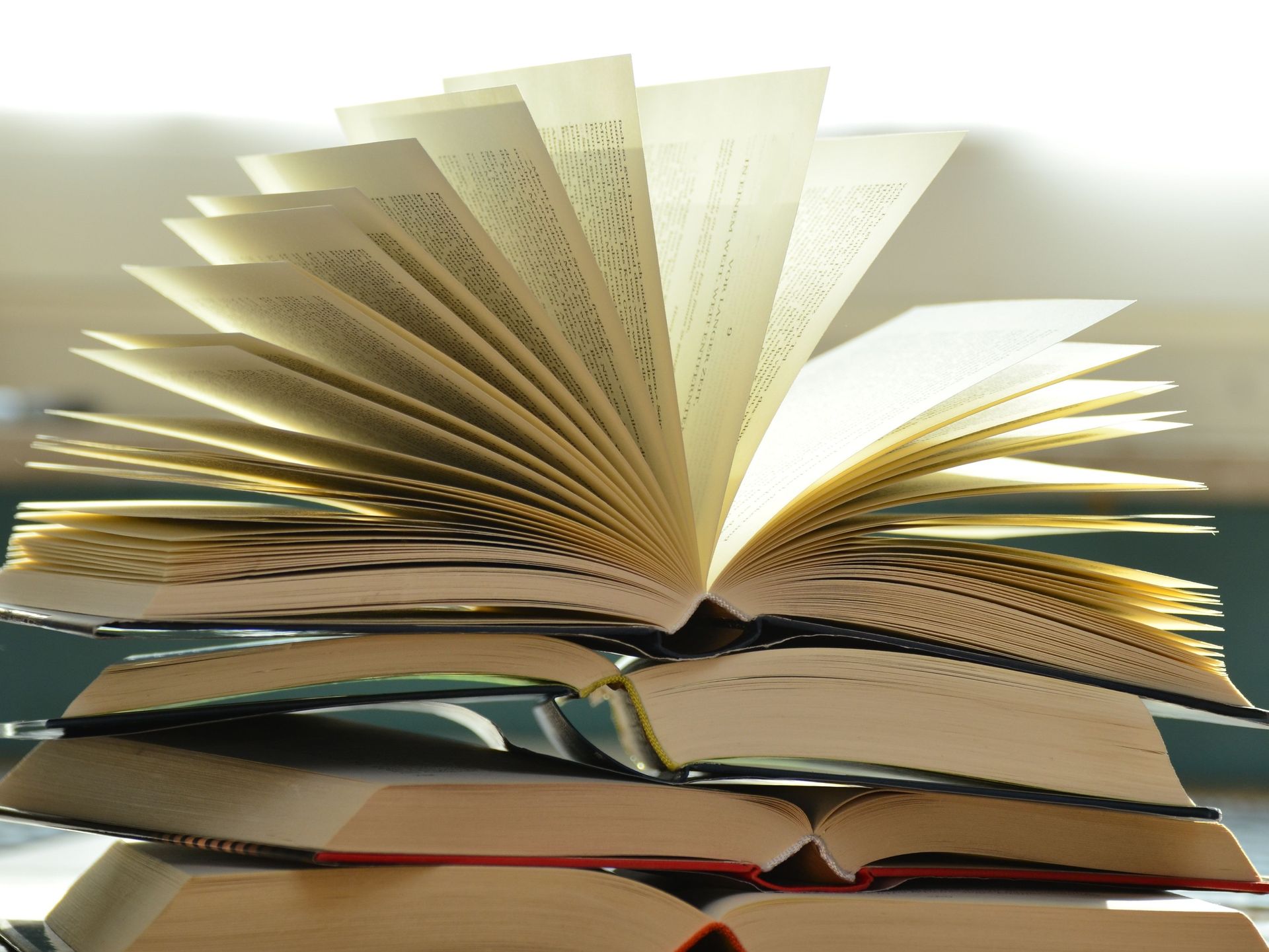 Pila de libros, uno de ellos abierto, con las páginas desplegadas. La luz brilla sobre las páginas, creando un cálido resplandor.
