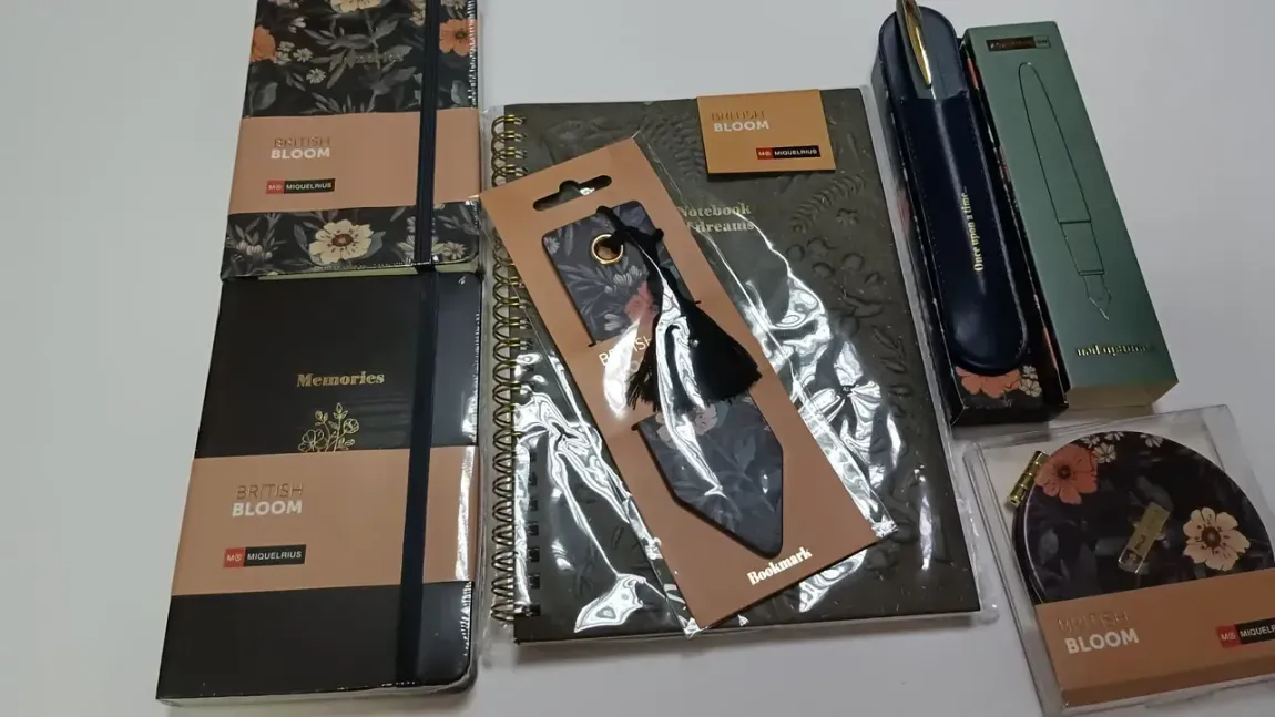 Juego de papelería con estampado floral que incluye cuadernos, bolígrafo, marcapáginas y posavasos sobre una superficie blanca.