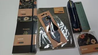 Juego de papelería con estampado floral que incluye cuadernos, bolígrafo, marcapáginas y posavasos sobre una superficie blanca.