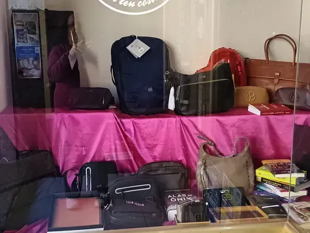 Escaparate con diversos bolsos y complementos, sobre una superficie drapeada en color rosa, detrás de un cristal.