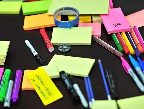 Varias notas adhesivas de colores, marcadores, bolígrafos y cinta sobre una superficie oscura, lo que sugiere una sesión de lluvia de ideas o de organización.