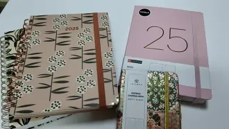 Varios cuadernos de distintos tamaños y diseños florales, incluido un planificador 2025 y un cuaderno rosa con el número 25.