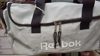 Bolsa de lona Reebok azul claro con asas y cremallera negras y logotipo blanco en la parte delantera.