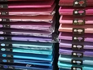 Pilas de papel de colores en varios tonos, incluidos rosa, púrpura, azul y rojo, exhibidos en una tienda.