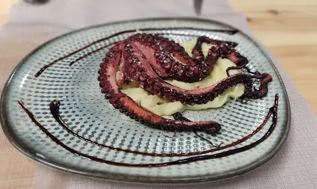 Un plato de comida con pulpo y puré de patatas en una mesa.