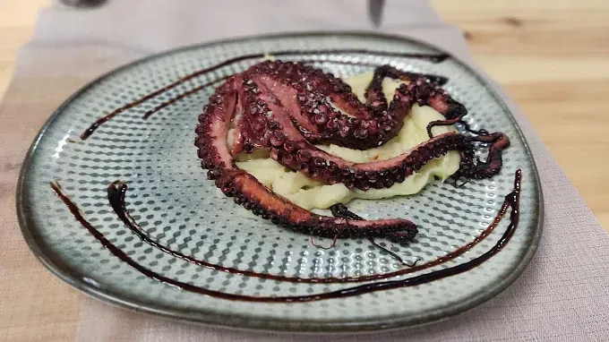 Un plato de comida con pulpo y puré de patatas en una mesa.