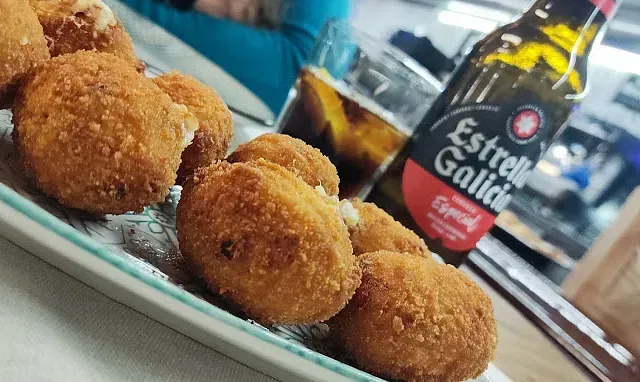 Una botella de cerveza Estrella Galicia está al lado de un plato de comida.