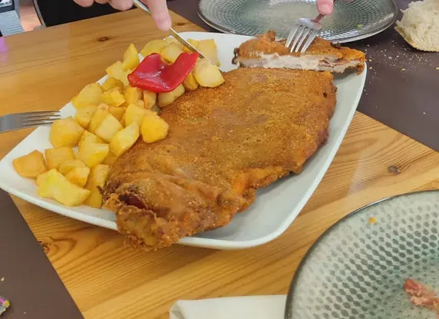 Un plato de comida con carne y patatas en una mesa de madera.