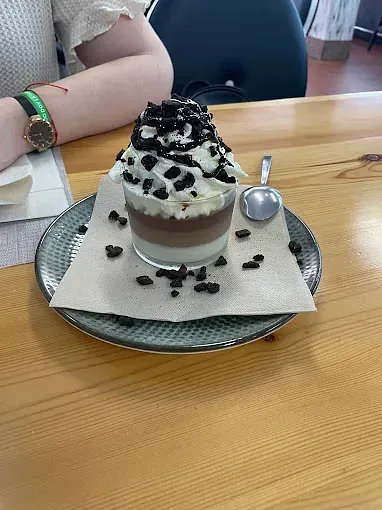 Un postre en un vaso en un plato con una cuchara sobre una mesa de madera.