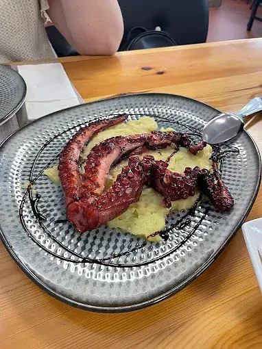 Un plato de comida con un pulpo y puré de patatas sobre una mesa de madera.