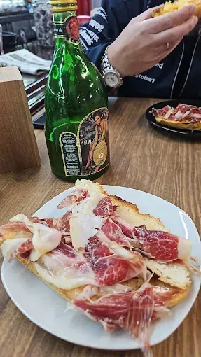 Una persona está sentada en una mesa con un plato de comida y una botella de cerveza.