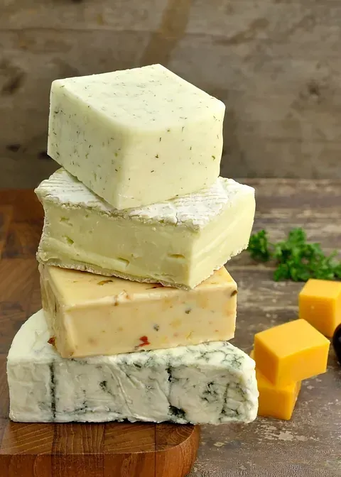 Una pila de diferentes tipos de queso en una tabla de cortar de madera.