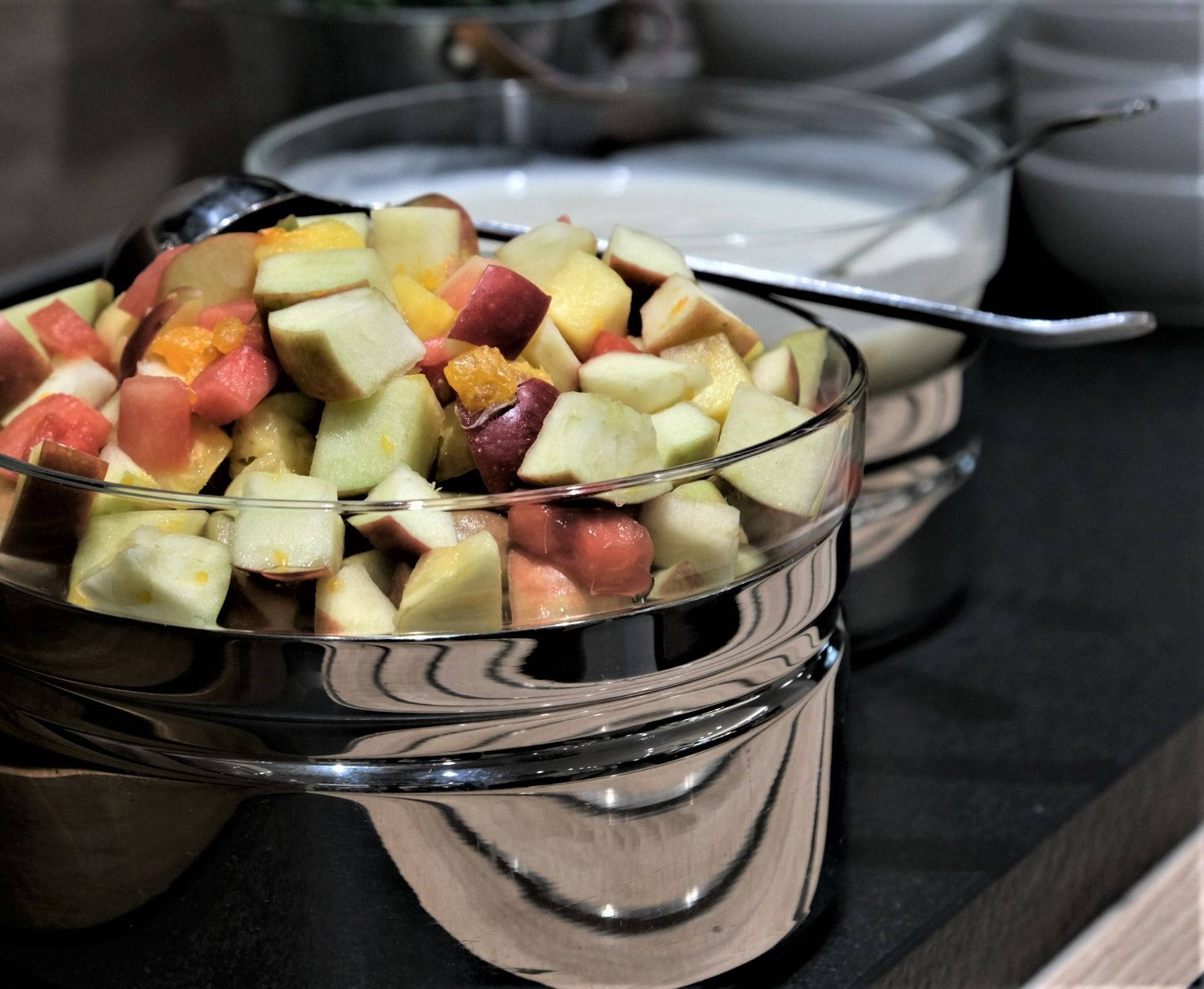 Obstsalat in einer Glasschale auf einem Buffet, im Hintergrund eine Schale mit weißem Joghurt.
