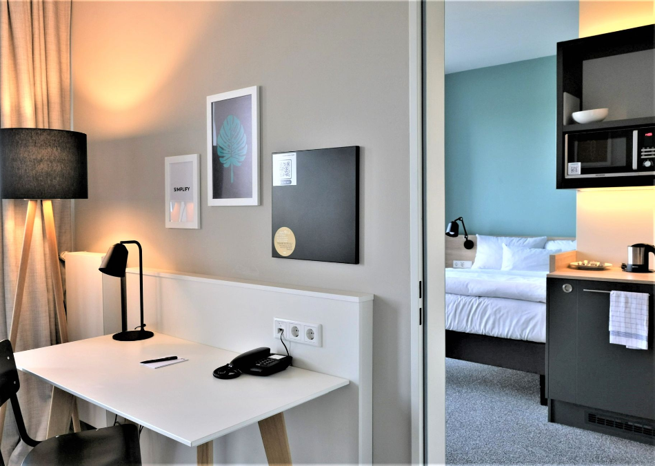 Ein Hotelzimmer mit Schreibtisch, Stuhl, Lampe und Mikrowelle.