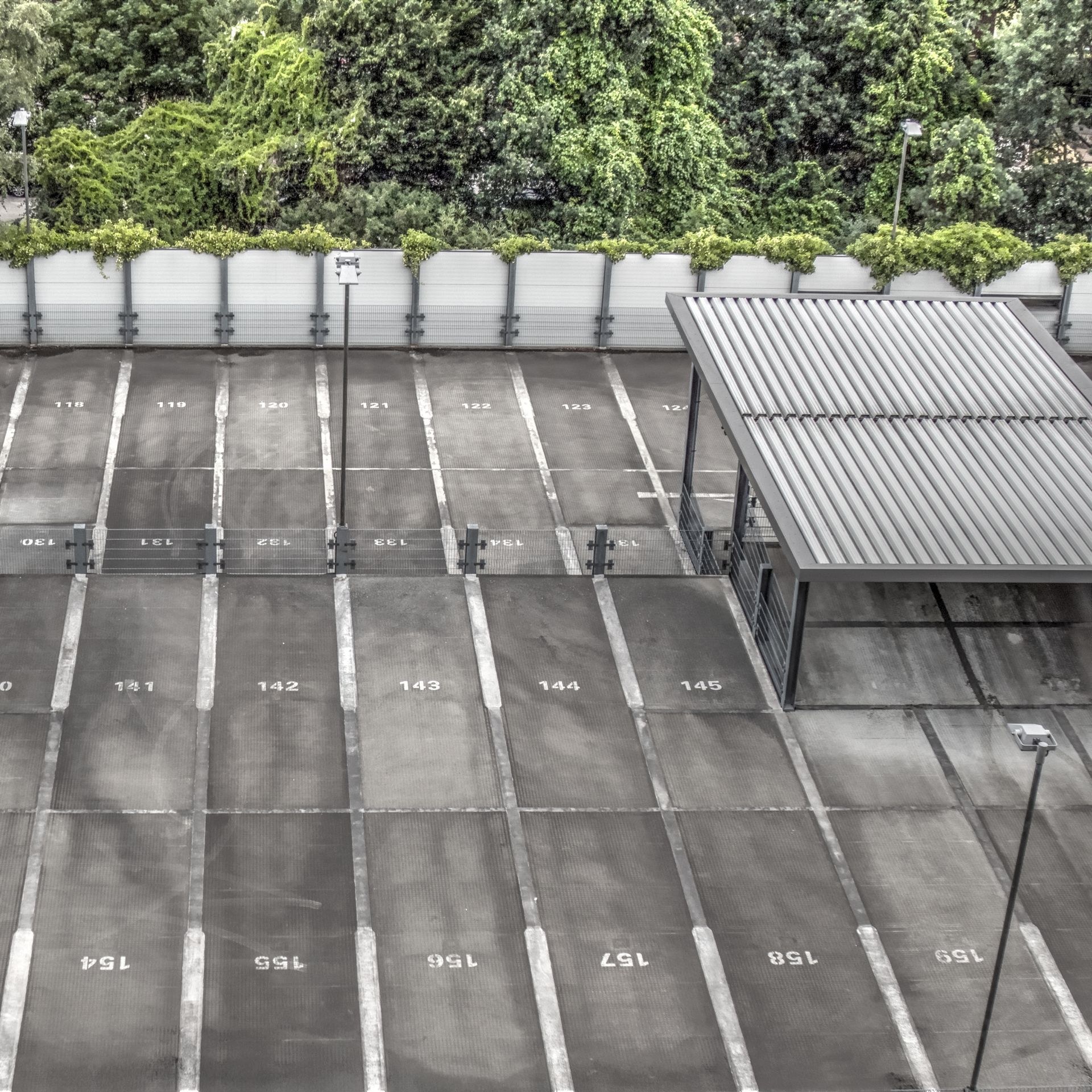 Overhead view of a mostly empty, numbered parking lot with a covered area and trees in the background.