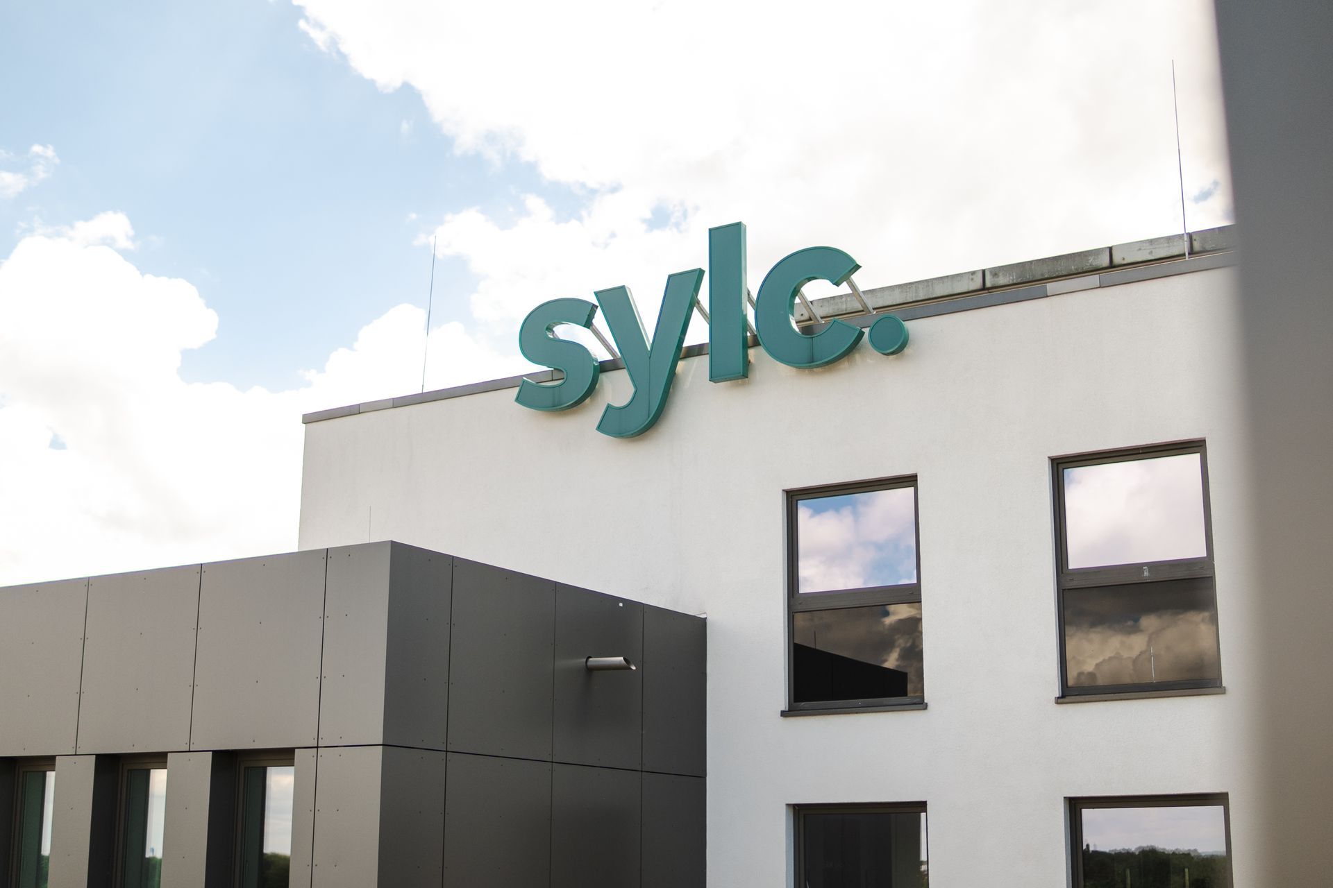„Sylic“-Schild auf einem modernen weißen Gebäude mit dunkelgrauen Akzenten und Fenstern vor einem bewölkten Himmel.