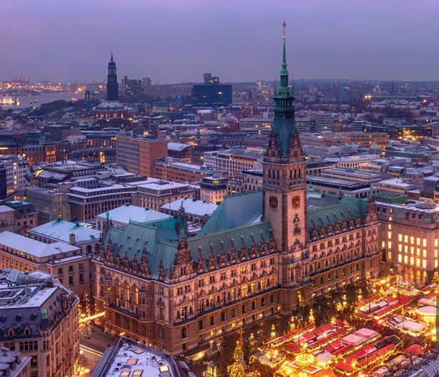 Das Hamburger Rathaus in der Abenddämmerung, schneebedeckt, darunter ein festlich beleuchteter Markt.