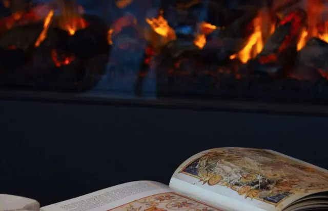 Eine Person liest vor einem Kamin ein Buch.