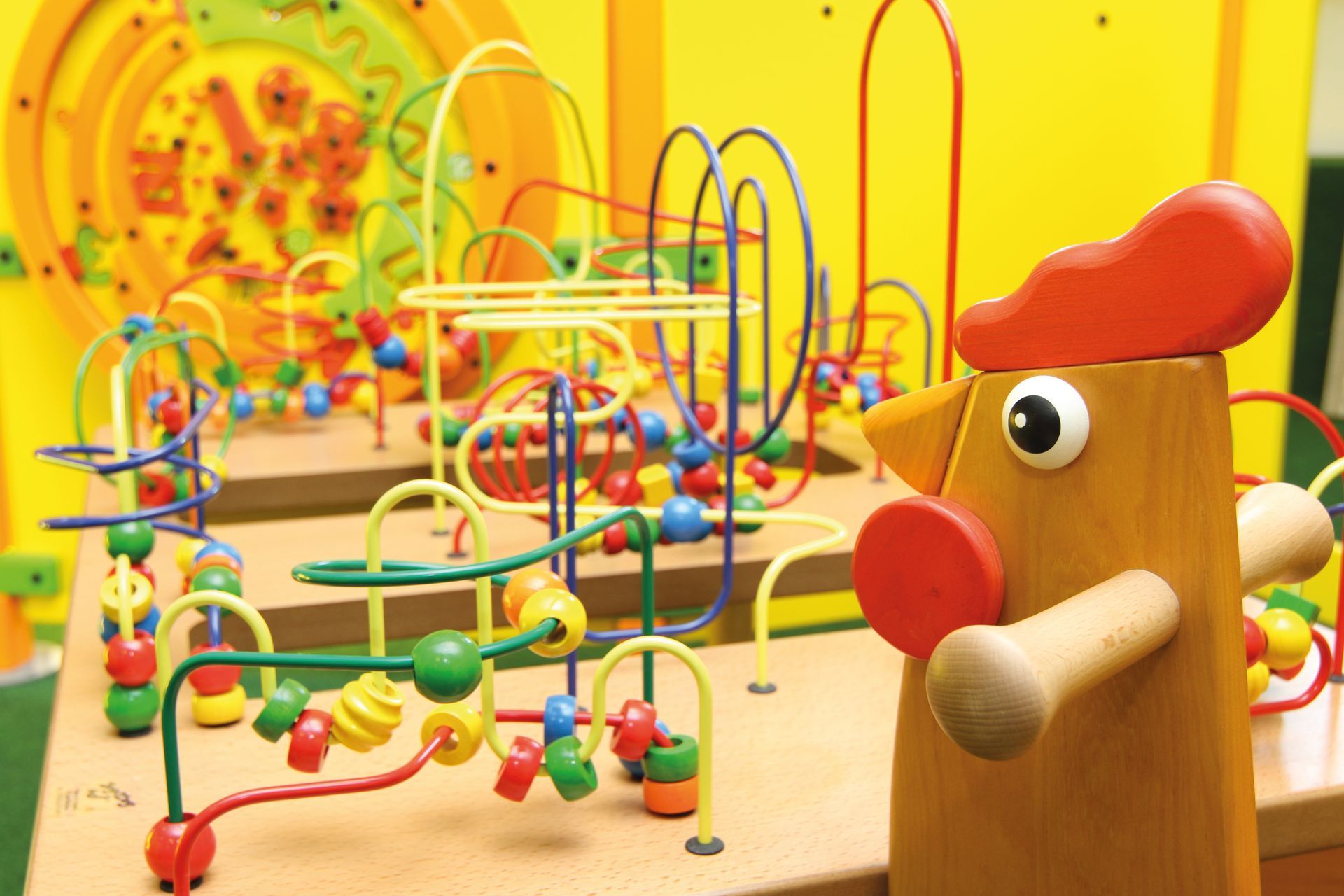 Ein Holzhahn steht vor einem Perlenlabyrinth.