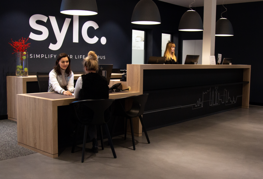 Zwei Frauen sitzen an einem Tisch vor einem SYLC-Schild.