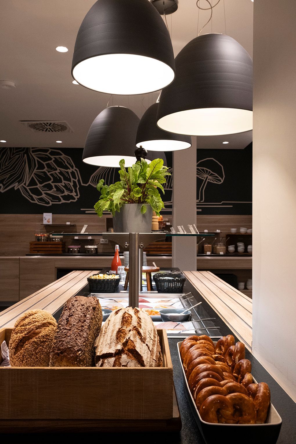 EATERY: Frühstücksbuffet mit frischem Brot und Gebäck unter schwarzen Pendelleuchten